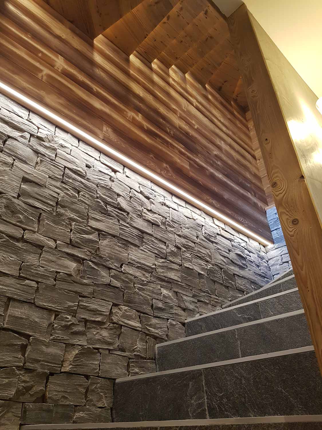 Poutres en bois de plafond dans un escalier avec un revêtement de mur en pierre.