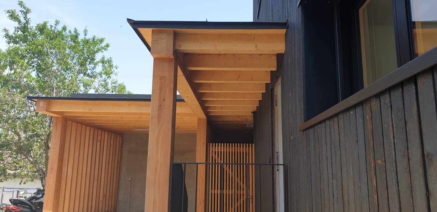 Charpentier installant une pergola en bois sur une maison moderne.