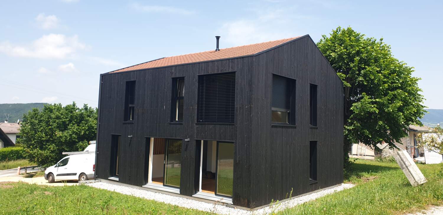 Construction de maison en bois moderne avec de grandes fenêtres et bardage noir.
