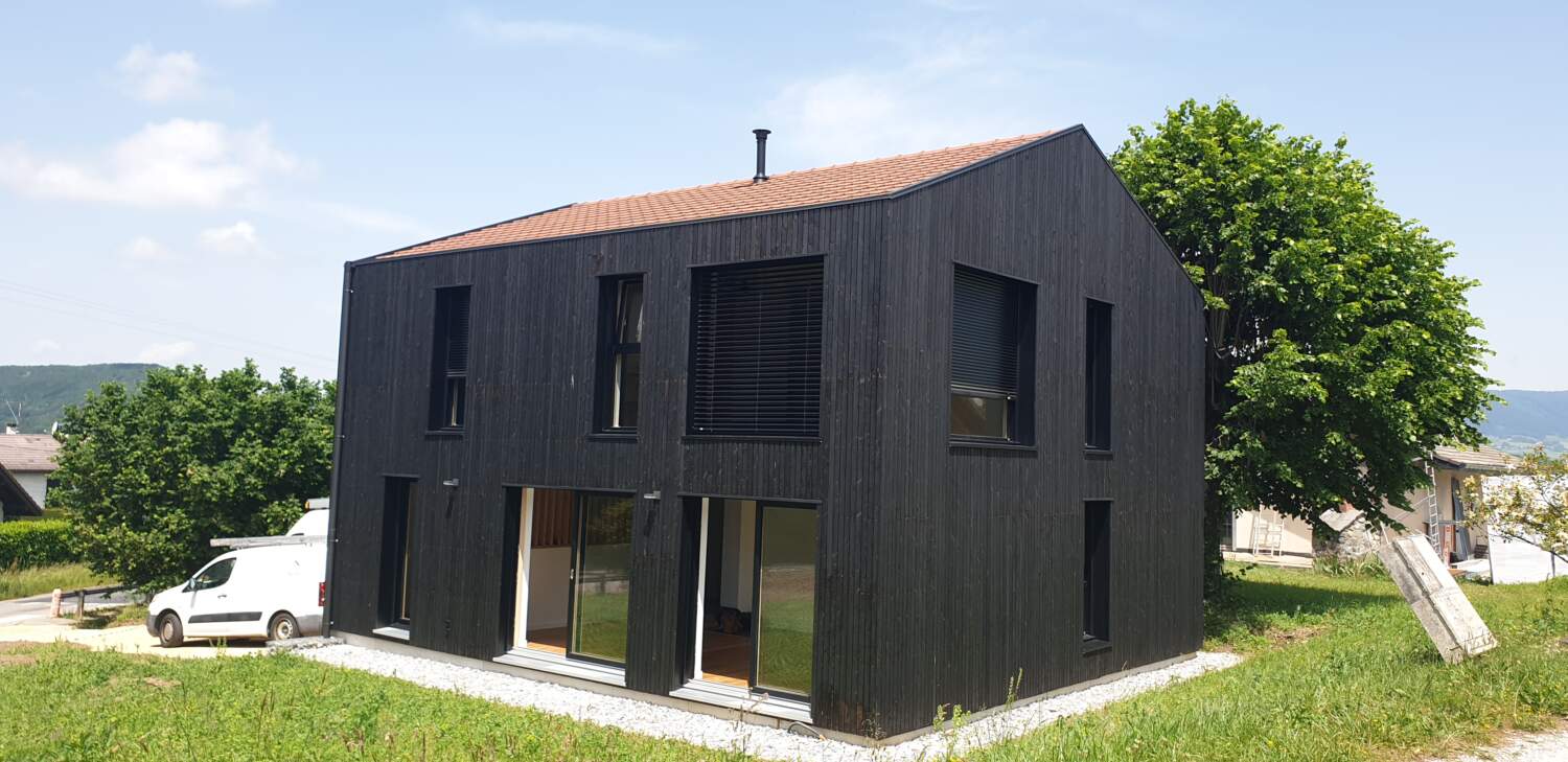 Maison moderne avec bardage en bois noir et grandes fenêtres en cours de construction.