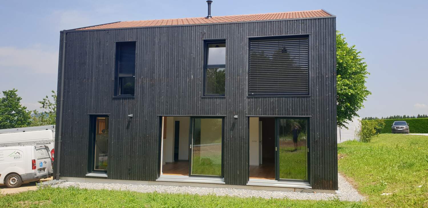 Maison moderne avec bardage en bois et grandes fenêtres en cours de construction.