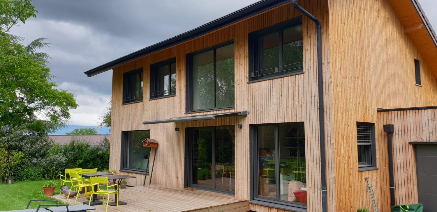 Extérieur de maison en bois moderne avec de grandes fenêtres et patio.
