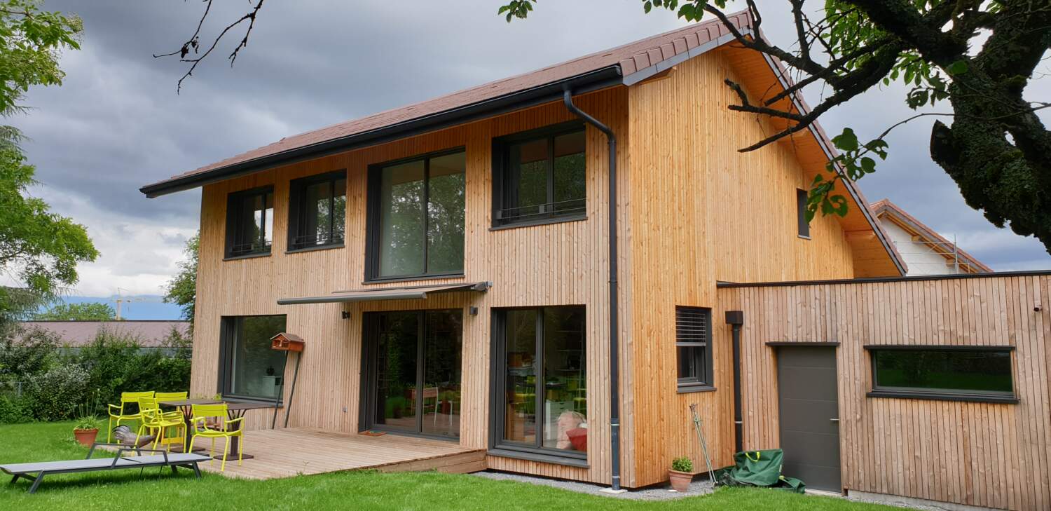 Maison en bois moderne avec de grandes fenêtres et patio.