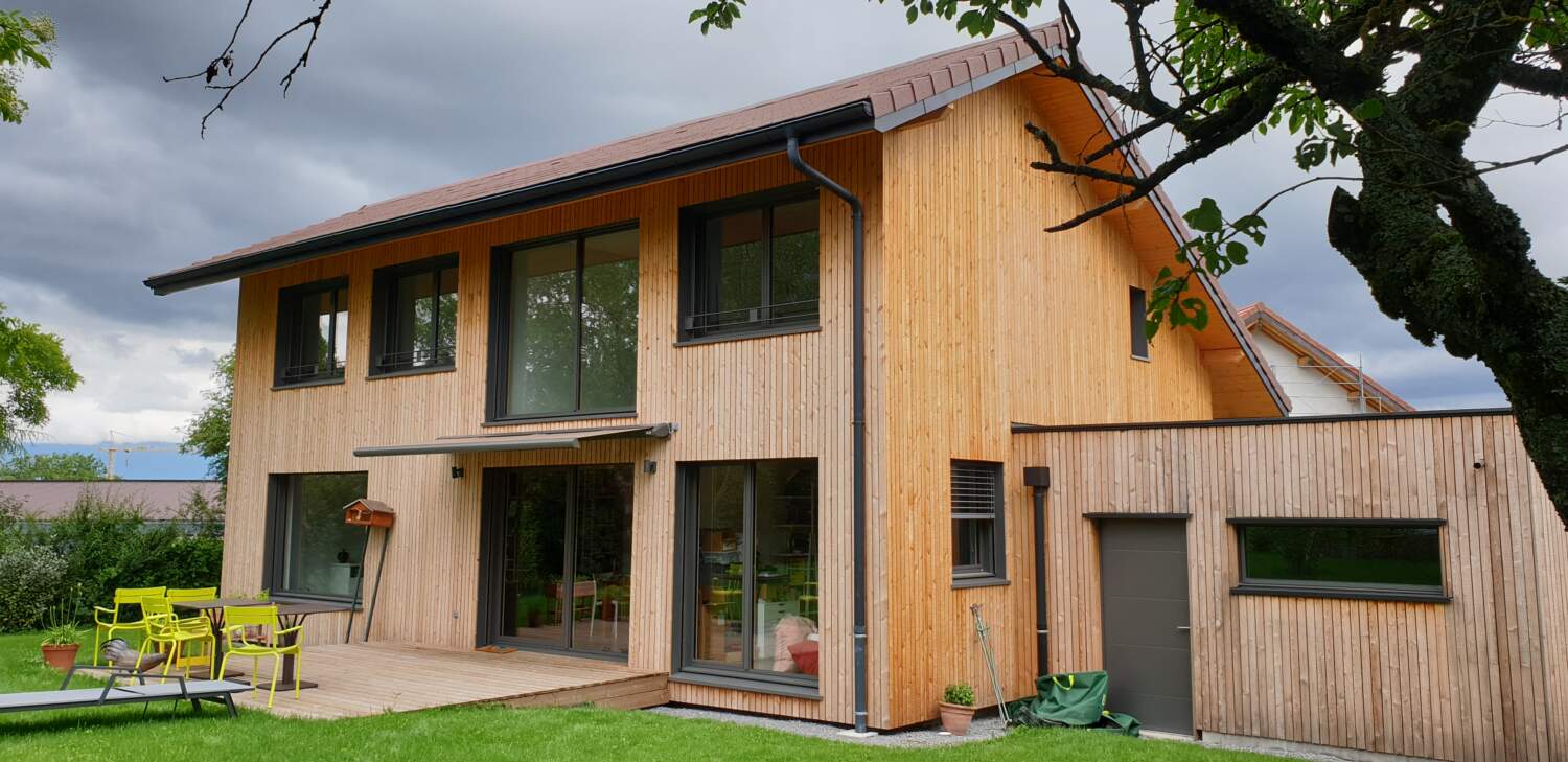 Extérieur de maison en bois avec de grandes fenêtres et un balcon.