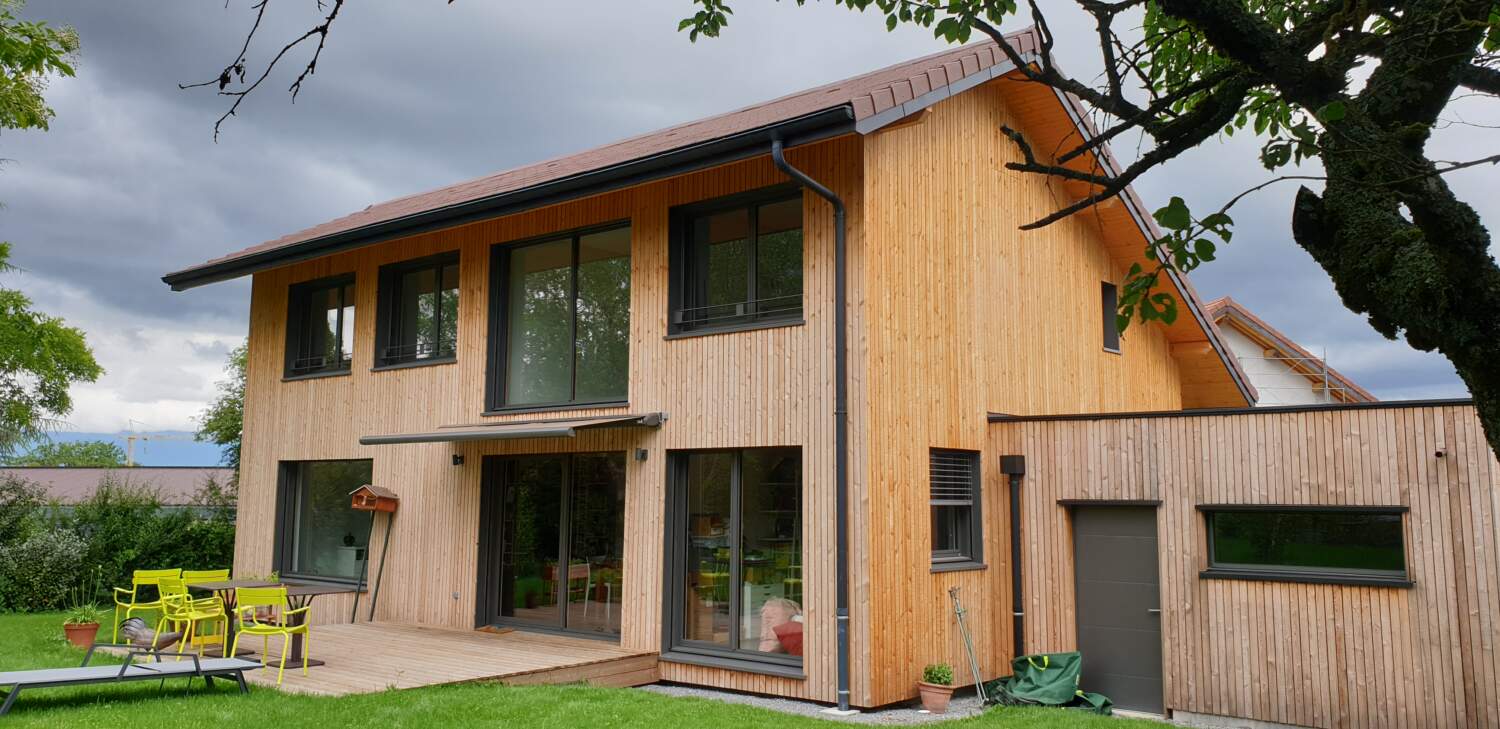 Extérieur de maison en bois moderne avec de grandes fenêtres et patio.