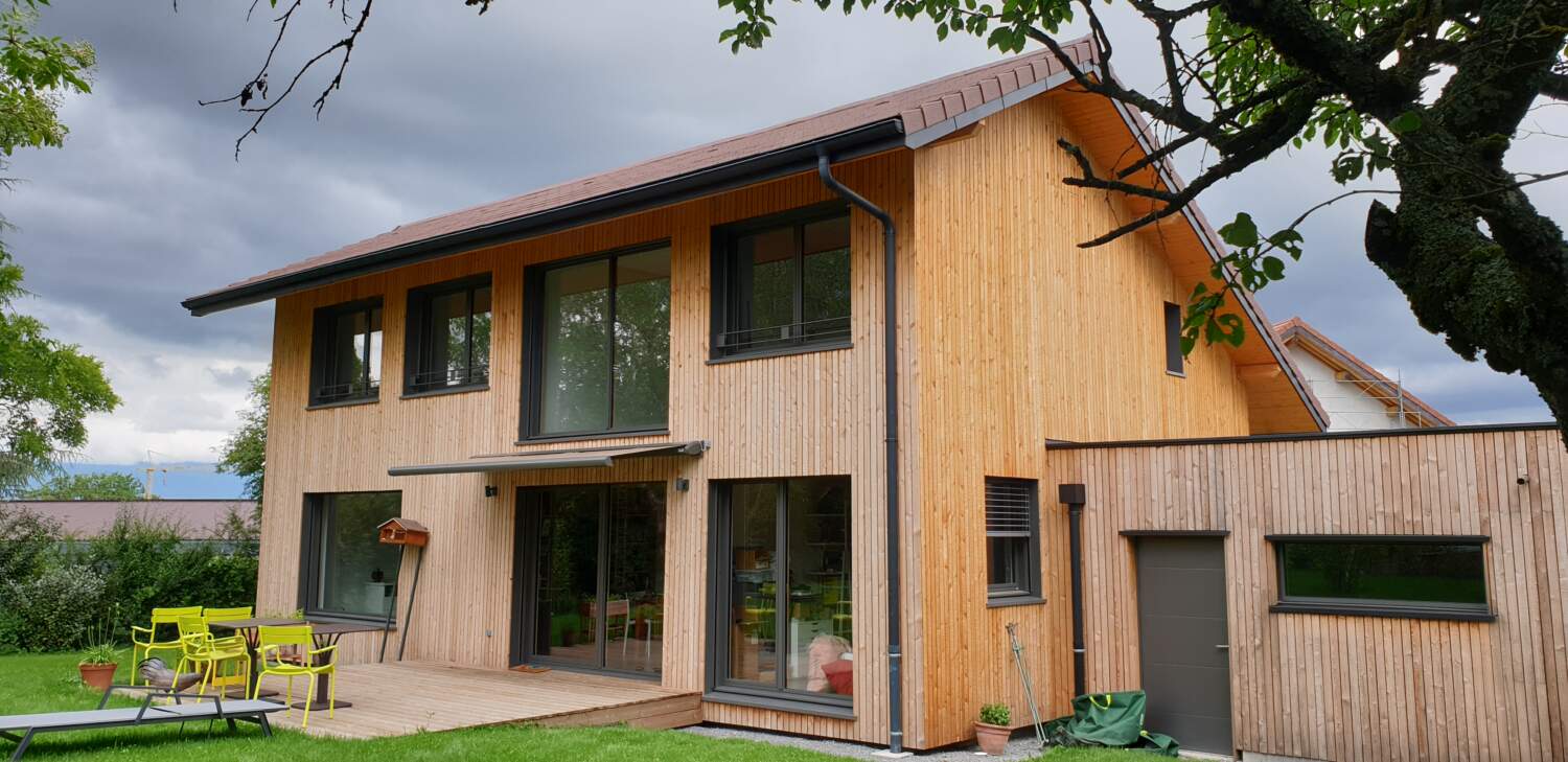 Extérieur de maison en bois moderne avec de grandes fenêtres et patio.