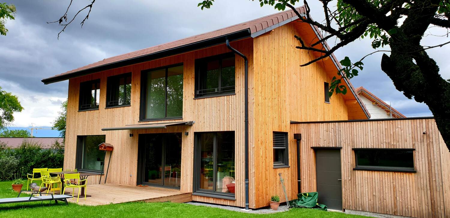 Extérieur de maison en bois moderne avec de grandes fenêtres et un balcon.