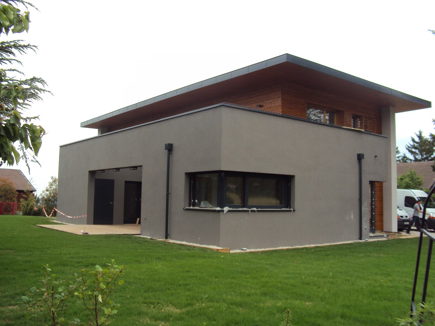 Construction de maison moderne avec murs gris et surplomb de toit en bois.